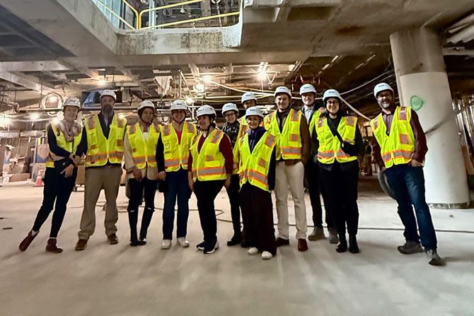 2025 AIA Strategic Council Report; A group of twelve people wearing yellow safety vests and hard hats pose inside a construction site. The environment is industrial and unfinished.