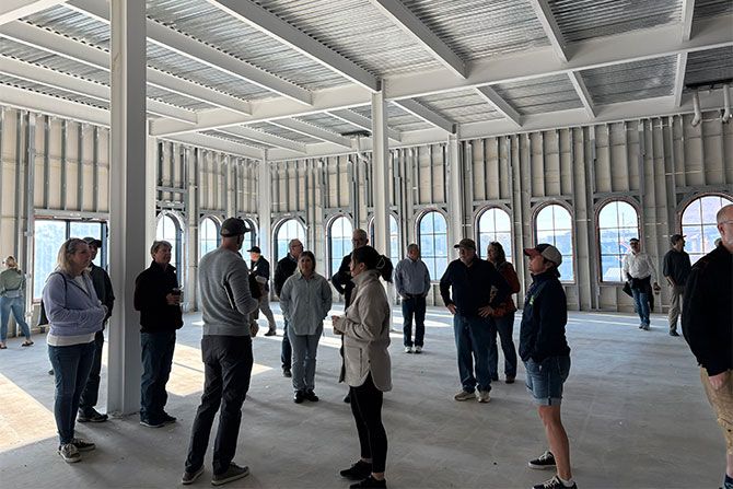 AIA Wyoming Annual Fall Conference: Reinvented — Rethinking What Currently Exists; A group of people stand and talk in a large, unfinished room with high ceilings and arched windows. The atmosphere is casual and light.