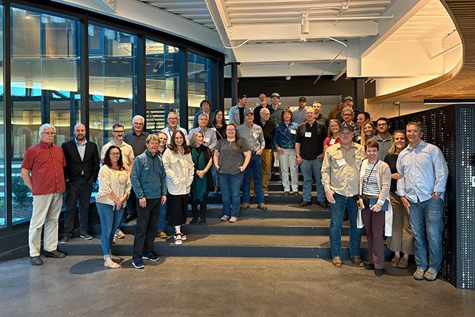 AIA Wyoming Standing Committees; A diverse group of approximately 35 people smiling and posing on indoor steps. The setting appears to be a modern office with large windows, conveying a sense of camaraderie and professionalism.