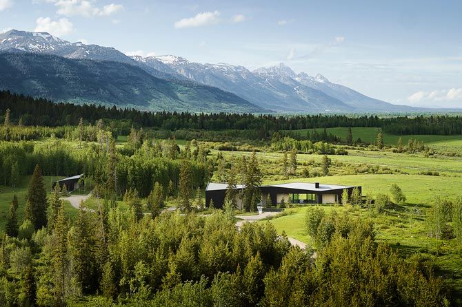 A modern house nestled in lush greenery with mountains in the background under a blue sky. Peaceful and scenic landscape, evoking tranquility.
