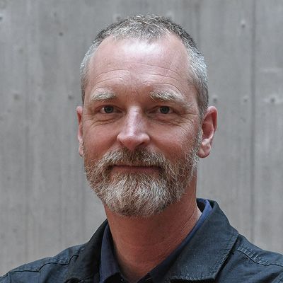 Erik Sommerfeld; A smiling man with short gray hair and a beard stands against a plain gray background. He wears a dark jacket, conveying a calm and approachable demeanor.