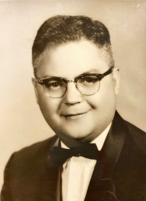 Portrait of a man in vintage attire with dark-rimmed glasses and a bow tie, smiling warmly. The sepia tone adds a nostalgic, classic feel.