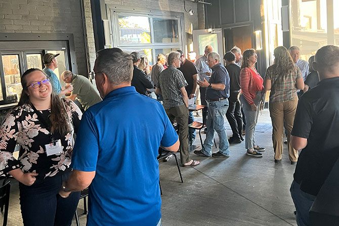 A group of adults socializing indoors at a networking event. People are dressed casually, chatting, some smiling, with a warm, friendly atmosphere.