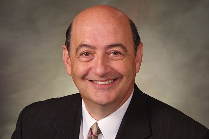 Stephan A. Pappas, A Renaissance Man; A smiling bald man in a suit and tie against a neutral background. His warm expression conveys friendliness and professionalism.
